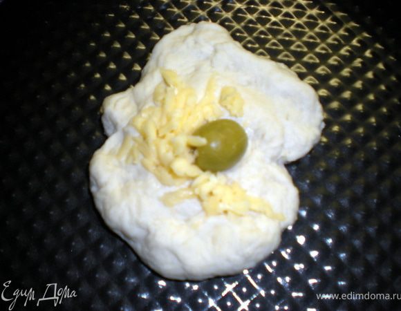 Тесто обмять и разделить на шарики.Каждый шарик размять руками в лепёшку и положить внутрь начинку из тертого сыра и оливки.