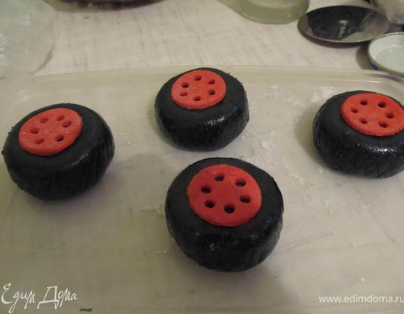 Из красной мастики вырезать маленькие кружочки, в каждом с помощью коктельной трубочки вырезать дырочки,и приклеить с помощью водки в центр каждого колеса. На колесах зубочисткой нанести рисунок шин.
