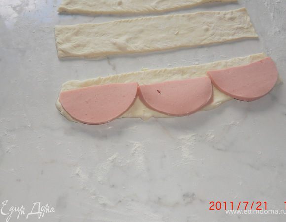 Колбасу режем тонко на колёса и делим пополам. Укладываем по 3-4 половинки на полоску, оставляя в конце немного места для подгиба.