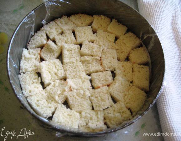 Разъёмную форму выслать пищевой плёнкой и выложить на дно бисквит.