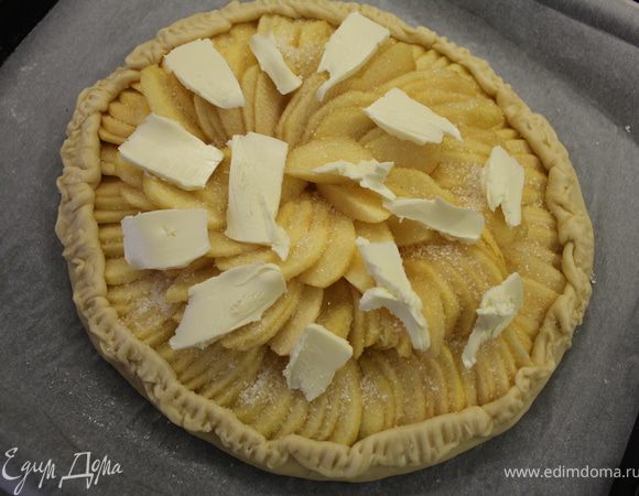 Посыпать яблоки сахаром, разложить кусочки сливочного масла и поднять края теста, сформировав бордюр. Выпекать 45 минут, пока яблоки не зарумянятся и не станут мягкими.