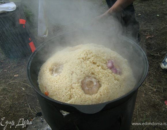 Убавьте огонь. Снимите крышку. Шумовкой соберите рис горкой. Сделайте в горке несколько проколов, воткните головки чеснока. Накройте крышкой и тушите на медленном огне 15 минут. Огонь должен быть слабым.