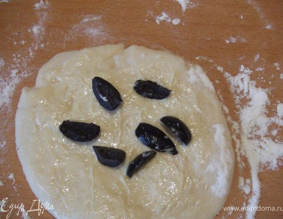 Шарики раскатать тонкую лепешку, смазать ее растопленным сливочным маслом, распределить щепотку оливок, немного вдавливая их. 