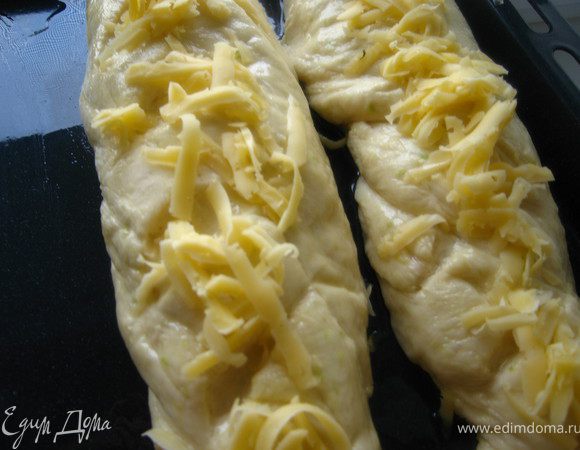 Кладем на противень смазанный маслом и зубчатым ножом вдоль делаем неглубокие надрезы. Оставляем для подъема. Затем смазали маслом и присыпали тертым сыром.