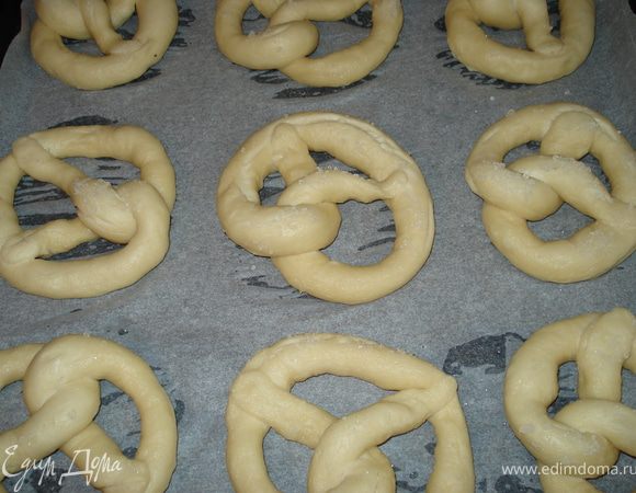 Вытащить брецель большой шумовкой ( только не алюминиевой ) и разложить на противень, застеленный бумагой для выпечки (лучше всего брать не бумажную , а многоразовую которую можно мыть или силиконовый коврик, а то брецели к бумаге прилипнуть могут), или же смазать противень маргарином. Сверху брецель слегка разрезать и теперь можно посыпать крупной солью, или сезамом, или маком, или же тёртым сыром. Выпекать 15 мин, до красивого цвета.