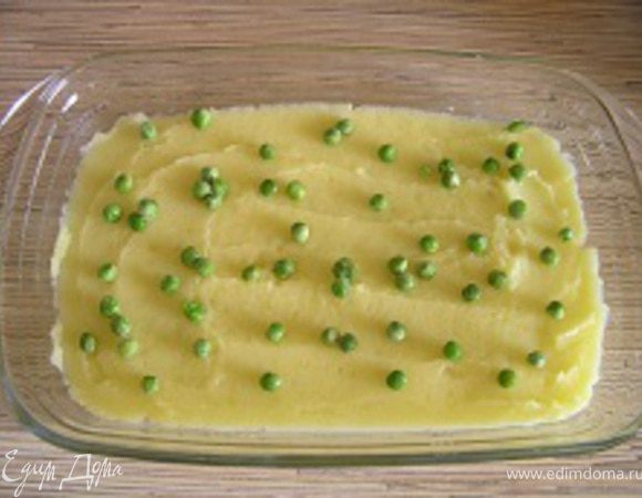 Форму для запекания смазать растительным маслом, выложить половину приготовленного пюре, посыпать горстью зеленого горошка.