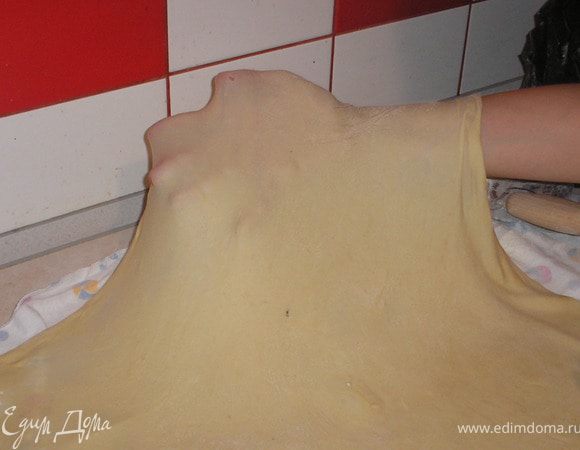 На большом куске ткани (у меня детская пеленка), предварительно посыпанном мукой, раскатываем очень  тонко наше тесто в форме четырехугольника. Помогаем себе тыльной стороной рук, растягиваем тесто.