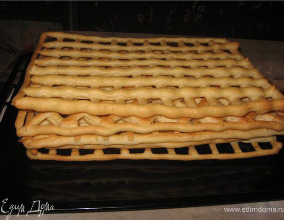 Берем 2 листа бумаги для выпечки рисуем карандашом по размеру блюда, контур. Его надо заполнить клетками 3х3 см, один прямо, другой косо.
Тесто кладем в кондитерский мешок или в пакет молочный с тонко отрезанным уголком и выдавливаем сначала контур , затем начинаем заполнять середину, тесто выдавливаем не толсто, в духовке оно увеличится в объёме. Листы с тестом кладем на противень. Выпекаем в духовке при 200 град. до легкого золотистого цвета, В это время делаем точно такую заготовку, но уже клетки по диагонали. Надо 4 коржа, 2 прямых, 2 косых.