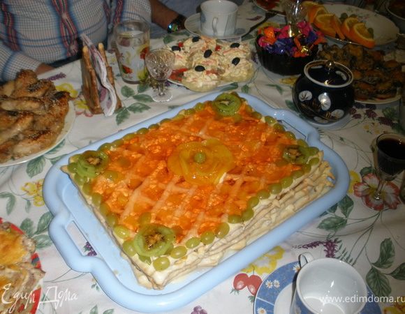 На блюдо для подачи положить первую решетку и в пустоты разложить кусочки фруктов на ваш выбор, подойдут любые: апельсин, банан, яблоки, виноград без косточки, смородина, вишня, персик. Сверху смазать кремом. Положить следующую решетку и так далее.
Верх торта смазать кремом и поставить в холодильник, чтобы крем немного застыл.
Затем верх торта украсить тонко нарезанными фруктами и залить прозрачным желе ( я прозрачный не нашла, взяла апельсиновый 2 пакета). Торт хранить в холодильнике, он должен пропитаться.
И вот что у меня получилось! Прошу прощения за основное фото, сама сфотографировать не успела, это муж в последний момент на столе сфоткал.