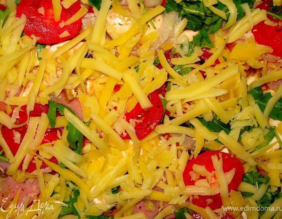 Теперь равномерно распределим начинку. Ломтики ветчины, сладких томатов, грибы, колечки лука. Присыпим все щепоткой сухого базилика и черного перца. Далее порвем половину нашей рукколы, поверх выложим сыр чеддер, натертый на крупной терке.