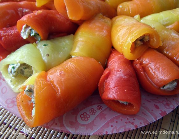 На подготовленную половинку перца выложить примерно столовую ложку начинки, свернуть рулетиком. Укладывать их на тарелке по кругу близко друг к другу, тогда рулет не развернётся. Готовые рулетики оставить охлаждаться до нужного момента.