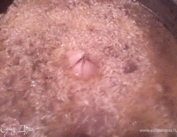 Рис хорошо промыть, выложить сверху на мясо и разровнять. Залить сверху горячей водой, так что бы она покрывала рис на пару сантиметров. Посередине воткнуть головку чеснока. А так же проделать дырочки для выхода пара. 