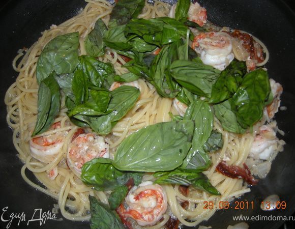 Воду вскипятить, подсолить и положить спагетти варить.Лук и чеснок мелко порубить и цуть обжарить на оловковом масле. 
Добавить креветки и обжарить до розового цвета.
Добавляем стакан белого вина и ждем когда оно цуть выпарится (пару минут).
Следующими отправляются вяленные помидоры. Если есть масло от них, отправляем и его в сковороду. Посолить, поперчить по вкусу.
К этому времени паста отварилась, отбрасываем на дуршлак и бросаем к креветкам. Осторожно перемешаем всё и снимаем с огня. 
В конце бросаем горсть свежей Рукколы и Базилика. Подавать к столу.