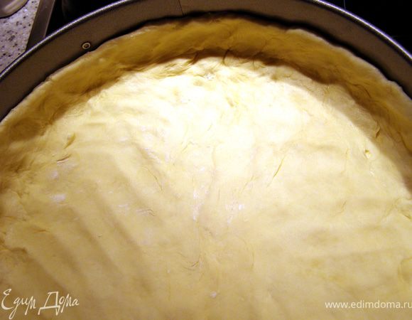 Охлаждённое тесто раскатать в круг, диаметром больше формы. Выложить тесто в форму, опуская руки в подготовленную тарелочку с мукой, чтобы оно не липло. Распределить тесто по дну и бортикам руками тонким слоем. Я брала форму 26 см, пирог получился не слишком высоким, если брать форму меньшего диаметра, пирог будет более высоким и нужно больше времени для запекания.