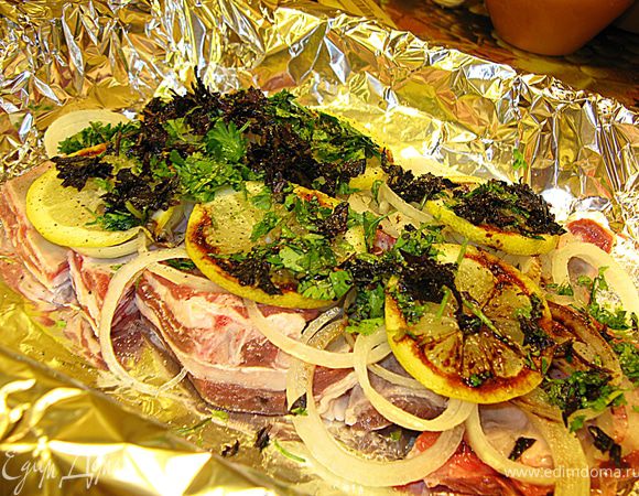 На противень щедро растилаем фольгу, я соединяла два полотна, чтобы было шире. Кладем первый слой бараньих ребрышек (кореечки), сверху нарезанные колечки лука, лимон (тоже колечками), нарубленную зелень, перчим, сбрызгиваем столовой ложкой соевого соуса.