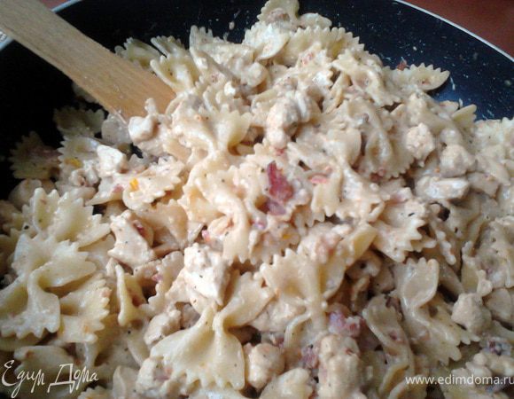 В обжаренную с беконом и травами курицу влить сливки и прогреть содержимое пару минут, как только начнёт закипать, сразу выключить плиту. Добавить крупно натёртый твёрдый сыр и пасту, всё смешать так, чтобы паста была однородно покрыта соусом. Оставить под накрытой крышкой на 5 мин.