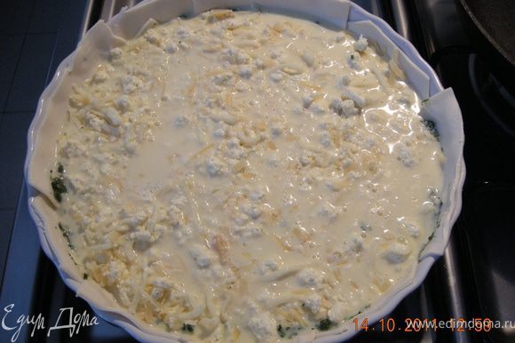 На тесто выложить остывший шпинат, сверху засыпать сыром и всё залить яично-молочной смесью .