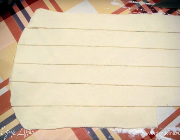 Тесто разморозить по инструкции и раскатать в одном направлении до толщины 0,5 см. Разрезать на полоски шириной 2 см и длиной 20 см.