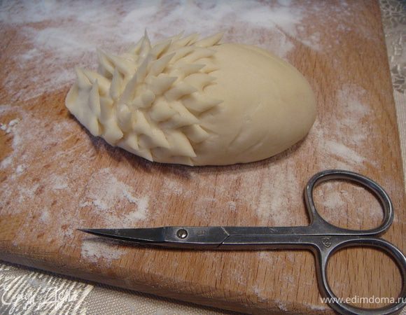 Из шариков сформировать овальные заготовки (туловище ежика). Один узкий конец заготовки сжать большим и указательным пальцами правой руки и сделать носик ежа. Затем взять маленькие чистые ножницы с тонкими лезвиями и, начиная от носика, сформировать иголочки: отщипнуть ножницами с одной стороны небольшой кусочек теста и поднять его вверх, устанавливая вертикально. 