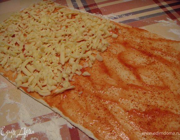 Разморозить тесто по инструкции. Раскатать пласт, толщиной 3 мм. Смазать его кетчупом, посыпать паприкой. На половину раскатанного пласта теста выложить натертый на крупной терке сыр.