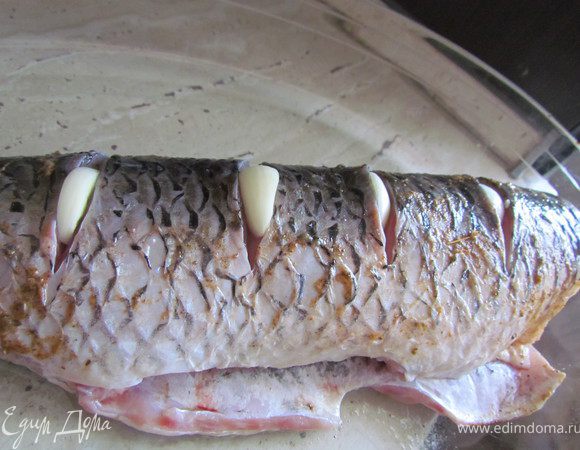 Сделаем глубокие поперечные надрезы на рыбе и нашпигуем их чесноком. Также немного чесночка положим внутрь рыбки и туда же положим пару маленьких лавровых листиков.