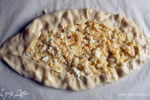 Сформировать "лодочку", часть сыра накрыв тестом. Взбить желток (можно добавить немного молока) и кисточкой смазать тесто.