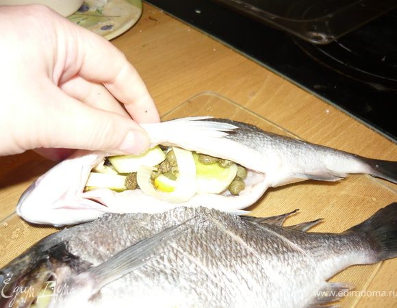 В брюшко положить по веточке розмарина, по пол зубчика предварительно раздавленного ножом чеснока, по несколько колечек лука порея, по пол кусочка лимона, по чайной ложке каперсов.