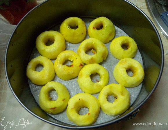 Яблоки почистить от кожуры и сердцевины. Порезать пополам и уложить срезами на дно формы. В форму предварительно застрелить бумагу и дно и стенки смазать растительным маслом.  