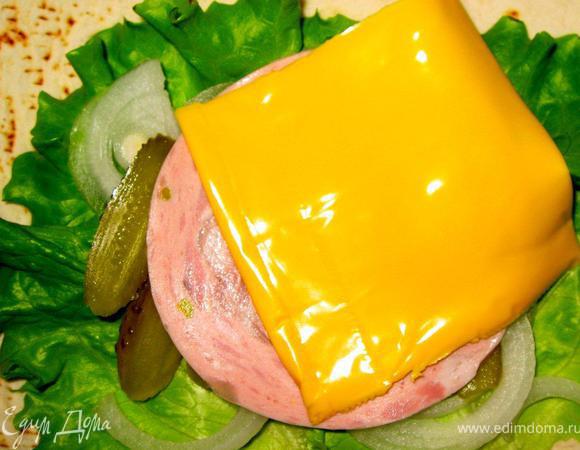 Поверх румяного бургера выкладываем тонкие колечки сладкого лука, ломтик колбасы мортаделла и еще один кусочек сыра чеддер. Из такого количества продуктов у нас получится 5 роллов. Пора их свернуть и довести до готовности.