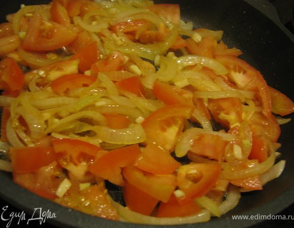 Лук порезать полукольцами и жарим в той же сковороде до золотистого цвета. Добавить нарезанные небольшими пластинками помидоры, измельченный чеснок и рубленную зелень петрушки.