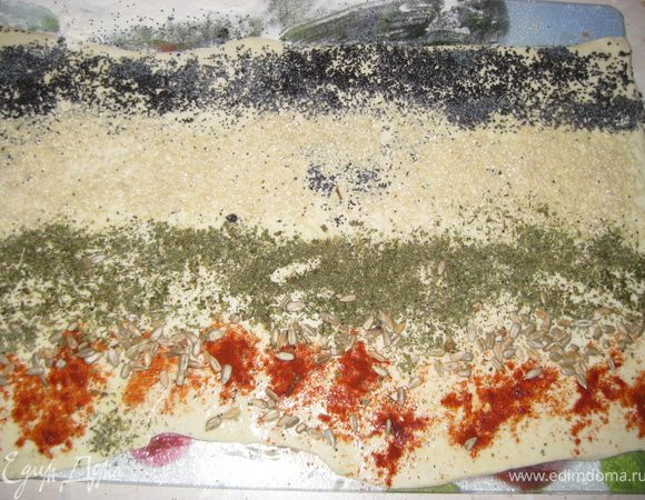 Готовим слоеные спиральки:
тонко раскатываем слоеное тесто,смазываем яйцом, поочередно, сверху-вниз полосой выкладываем на наше тесто сухой мак,кунжут, травки, подсолнечные семечки, паприку.