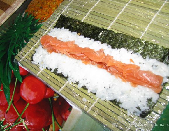 Выкладываем рис так, чтобы в конце осталась тонкая полоска листа нори. Именно эта полоска будет склеивать наш ролл. Посередине риса выкладываем нарезанную соломкой семгу.