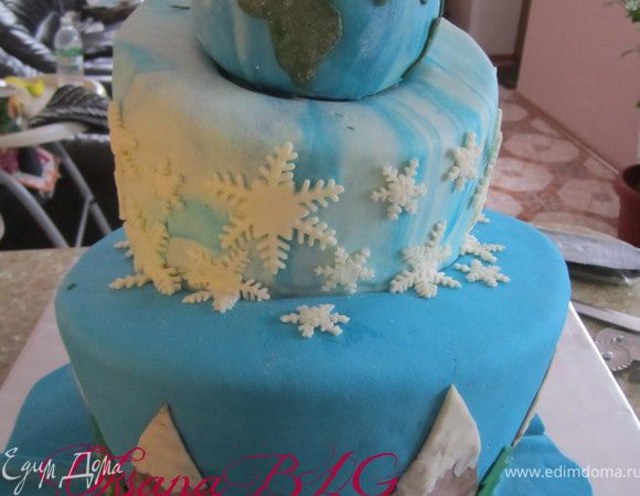 Поставить ярус на ярус, скрепив их немного масляным кремом. Торт нужно было транспортировать на небольшое расстояние, я для крепости по средине воткнула деревянную шпажку(30 см). Украшаем. На нижний ярус прикрепить "горы" из шокомастики и елочки из зеленой мастики. На второй ярус прикрепить снежинки, или нарисовать их айсингом.
