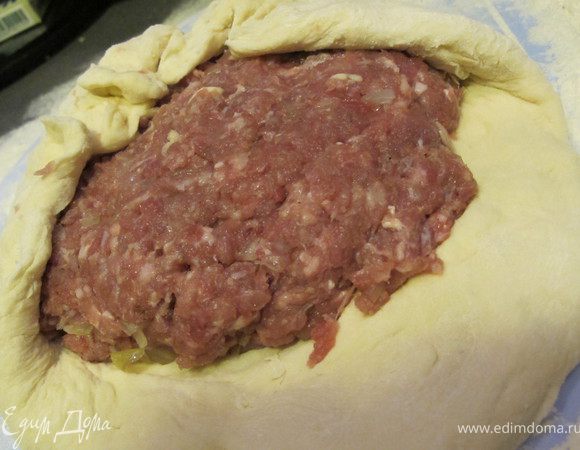Когда тесто поднялось, его надо обмять и тщательно вымесить с небольшим количеством муки и смазывая руки растительным масло. Разделить на 3 равные части. Из каждой руками сделать лепешки в центр которой положить мясную начинку (начинки должно быть много, почти так же как теста). Аккуратно собрать края к центру, присыпать мукой и ладонью примять, аккуратно распределяя начинку от центра к краям.Мы должны как бы раскатывать и растягивать лепешку руками Должна получиться лепешка диаметром 30-35 см.