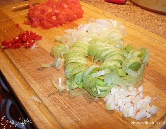 Овощи подготовим для жарки: лук-порей нарежем полукольцами, чеснок порубим, помидор освободим от кожицы, нарежем кубиком, перец чили освободим от семян и мелко нарежем