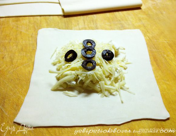 Слоеное тесто тонко раскатать, нарезать на квадраты. В центр квадрата выложить сыры слоями, не смешивая (филадельфию выкладывать чайной ложкой небольшими кусочками).