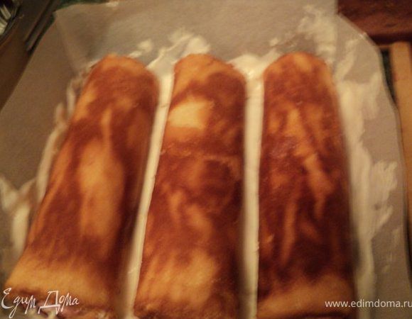 На бисквит выложить половину белого крема и сверху рулетики, немного притопив их в креме.