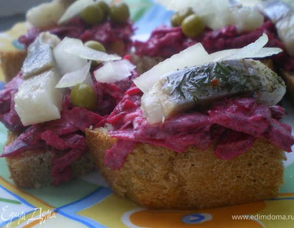 Кусочек любого тёмного хлеба разрезать на треугольники.Свеклу и чеснок натереть на тёрке, заправить майонезом и перемешать. Намазать на хлеб, сверху выложить филе сельди, украсить луком и зелёным горошком.