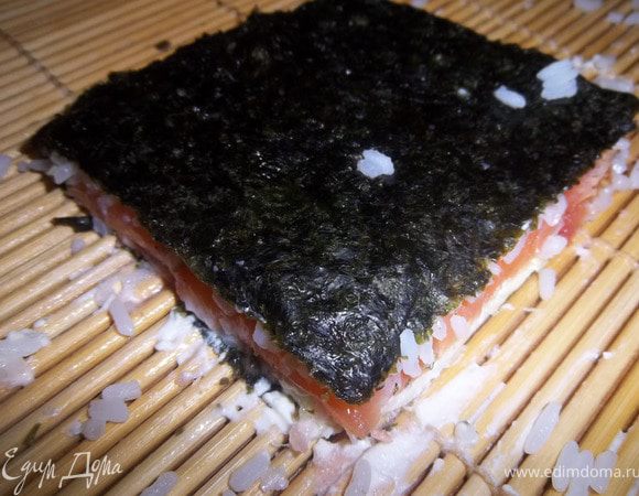 Приподнимая  кончик коврика, аккуратно накрыть свободной половиной листа нори, уплотняя содержимое.