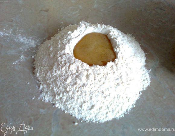 На стол высыпать муку, сделать углубление в центре горки и постепенно вливать туда смесь