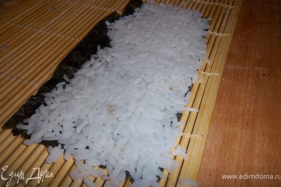 На край циновки положить лист нори и влажными руками выложить суши-рис.
