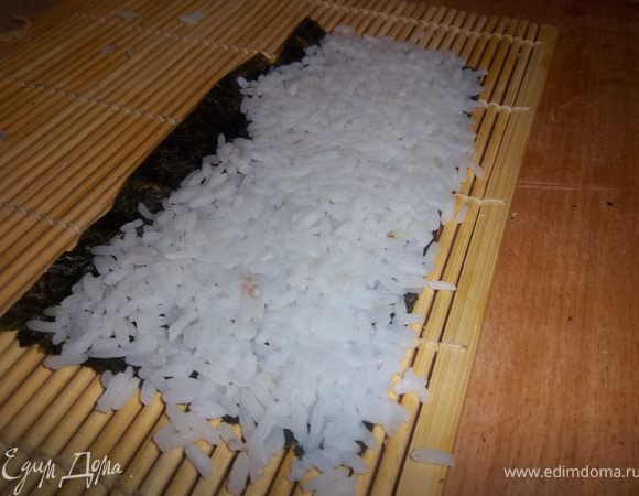 На край циновки положить лист нори и влажными руками выложить суши-рис.

