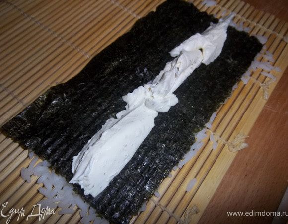 Убедиться, что рис хорошо утрамбован. Аккуратно взять за край и быстро перевернуть, чтобы рис оказался снизу. На середину нори выложить сыр «Филадельфия» (или любой другой сливочный сыр).