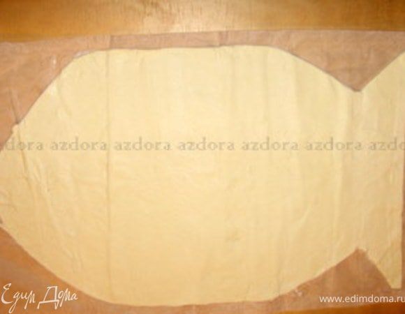 Взять слоёное тесто и вырезать из него рыбку. Для того чтобы вырезанная рыбка была симметричной и ровной, нарисовать на бумаге трафарет и по нему вырезать рыбку. Или же присыпать тесто мукой, сложить вдоль пополам, вырезать половину рыбки со сгибом в центре, развернуть.