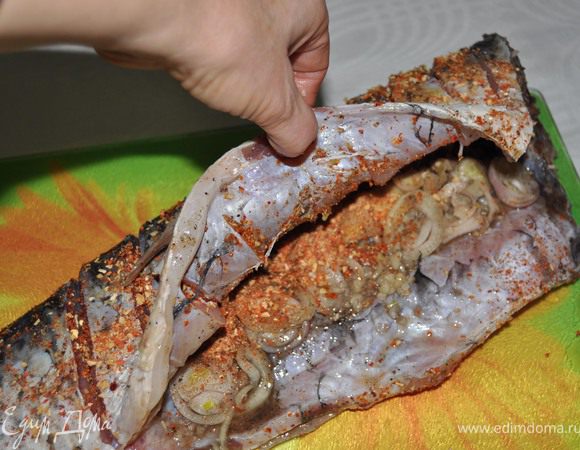 Натрите тушку чесноком, солью, приправами и перцем. Лук почистите, нарежьте кольцами и положите в брюшко рыбы.