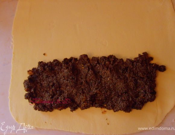 Заранее нагреем  духовку до 180 гр. Для этого достаем один кусочек теста.Если он у вас стало немного твердым, что понятно, пролежать ночь в холоде, можно постучать скалкой по нему, пока оно еще в пленке. Далее раскатываем его в пласт толщиной 2-3 мм, щедро посыпать мукой. После того как оно отдохнуло в холодильнике, оно становится почти шелковистым. Поэтому нужно быть очень осторожным, при переворачивании его. И на 1\4 часть выкладываем начинку из мака, загнув вовнутрь края, в виде рулета.