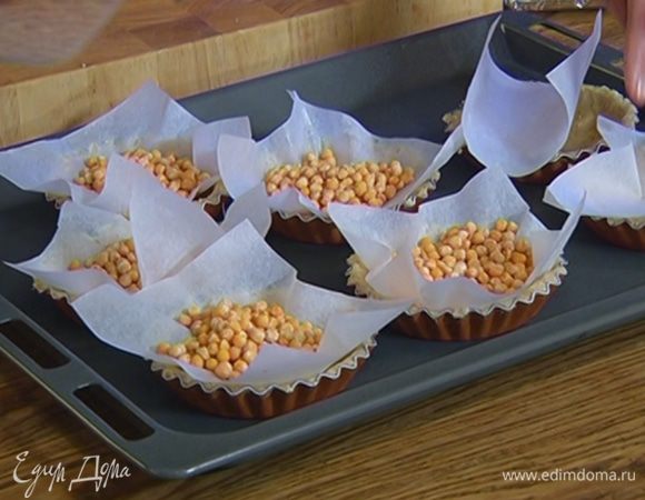 Вырезать из бумаги для выпечки квадраты чуть большего размера, чем формочки, положить их на тесто, сверху насыпать горох или фасоль.