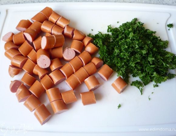 Нарезать сосиски кусочками, петрушку порубить.