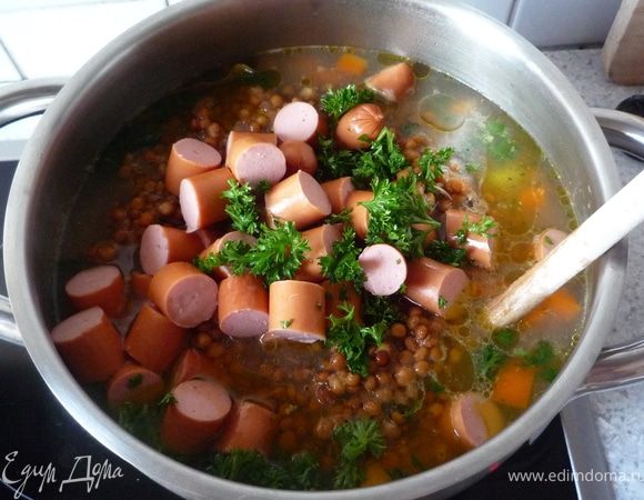 Добавить чечевицу с сосисками и петрушкой в суп, дать закипеть и потомить еще минут 5. При необходимости добавить горячей воды.