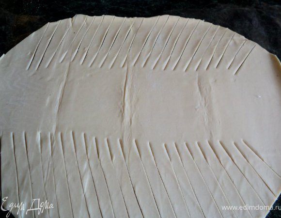 Готовый пласт слоеного теста слегка раскатать по краям, придав овальную форму. По краям теста с двух сторон сделать косые  надрезы.